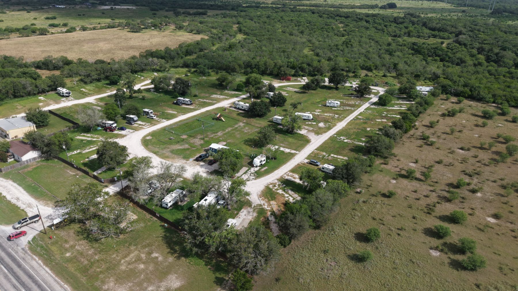 Aerial view across the interior gravel roads and open sites at The Texas Rose RV Park in Beeville, TX, with the park office at left