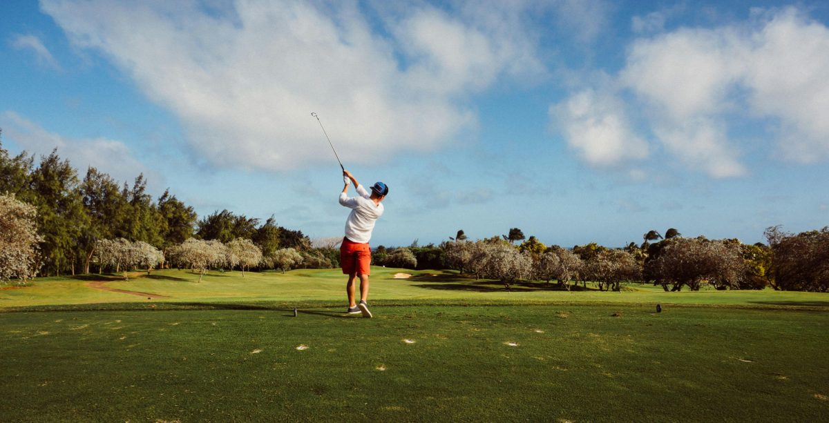 A golfer teeing off on a tree-lined fairway
