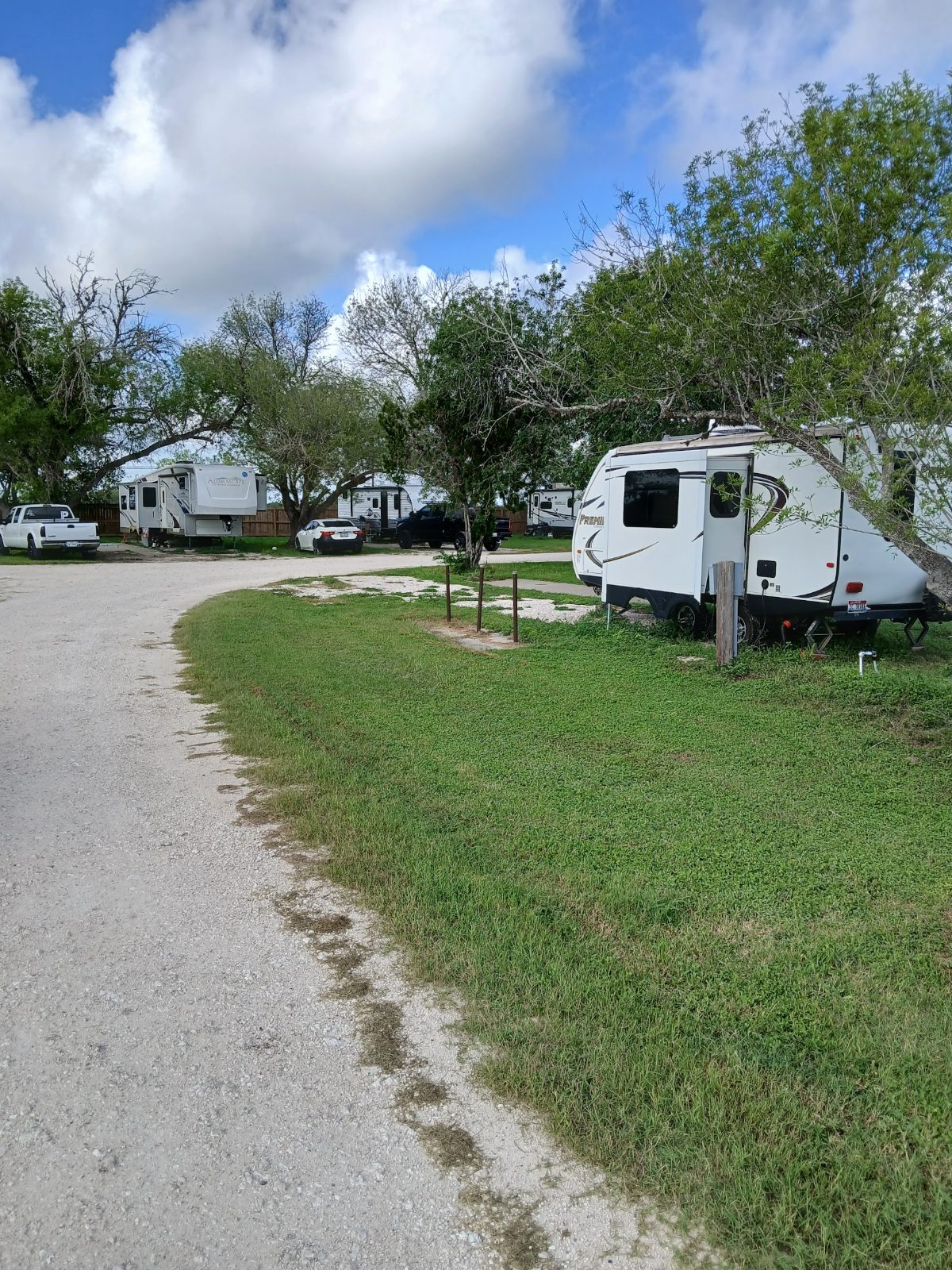 A wooden hookup post with electric box and water riser beside a travel trailer on a grass RV site at The Texas Rose RV Park in Beeville, TX